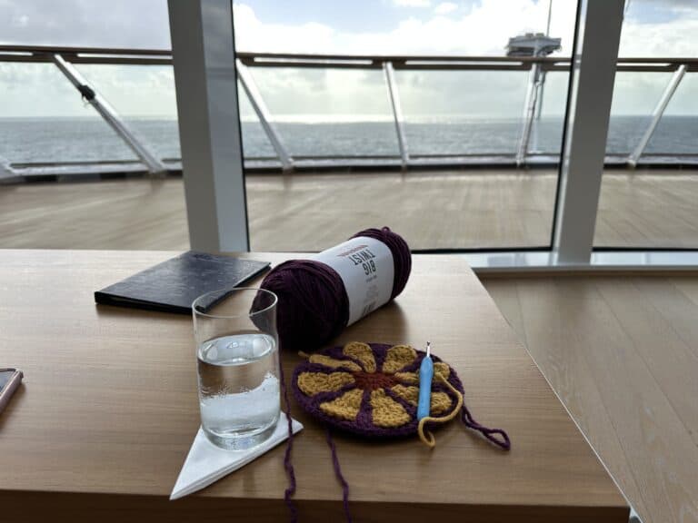 A spool of yarn and an crocheted flower sit on a table next to a glass of water overlooking the front of the ship. 